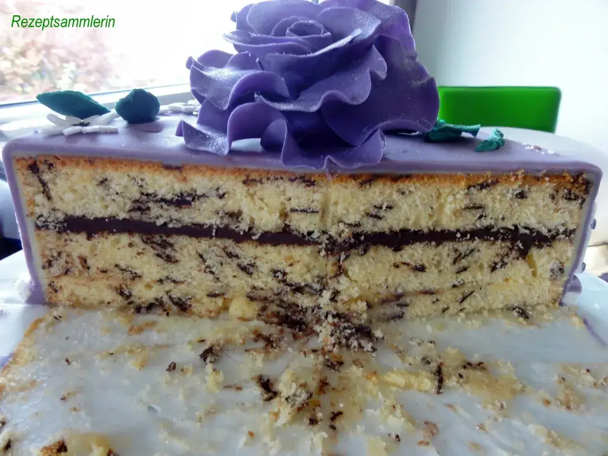 Anschnitt einer Stracciatella Torte mit Schokoladenfüllung, lila Fondant und einer großen lila Rose als Deko.