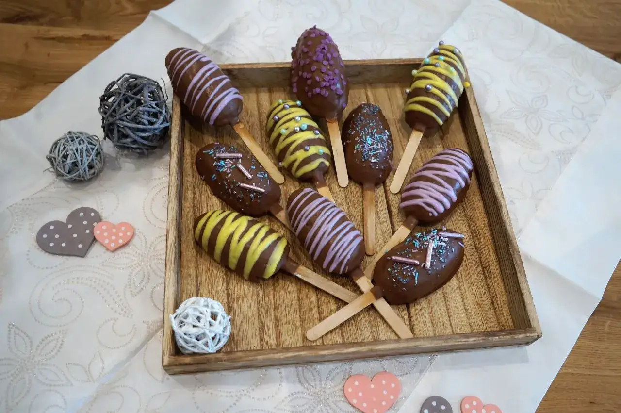 Schokoladige cake pops mit bunten Streuseln und Zuckerguss auf einem Holztablett, dekoriert mit Herzen.