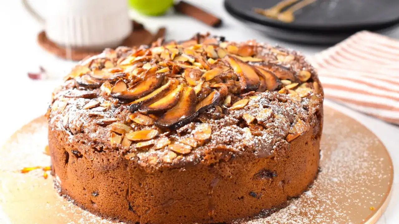 Ein köstlicher veganer Apfelkuchen, bestreut mit Puderzucker und garniert mit gerösteten Mandeln und karamellisierten Apfelscheiben.