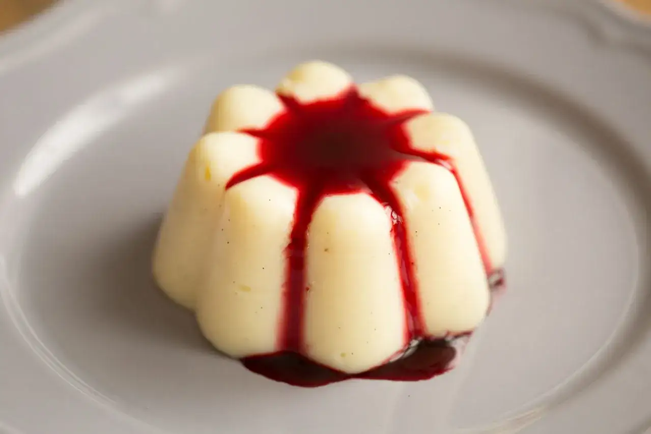 Ein selbstgemachter Vanillepudding, verziert mit rotem Beerensirup, auf einem grauen Teller.
