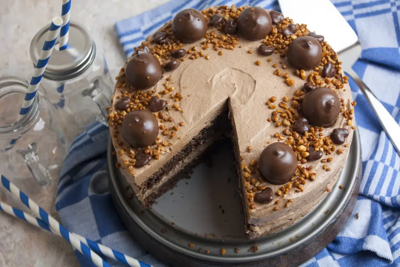 Schokoladige nougat torte mit Pralinen und Nüssen verziert, bereit zum Servieren mit blauen Strohhalmen.