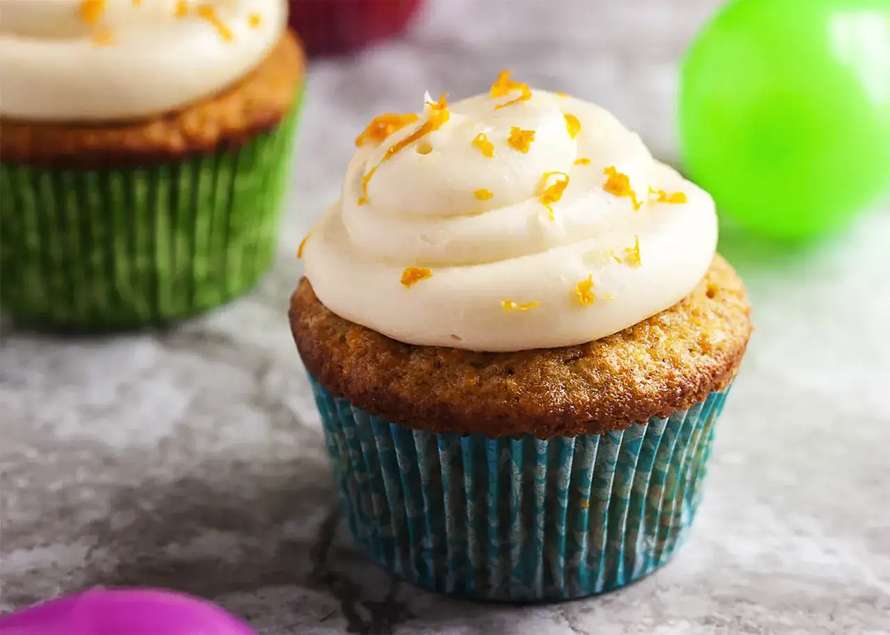 Saftige karotten muffins mit cremiger Glasur und Orangenschale bestreut.