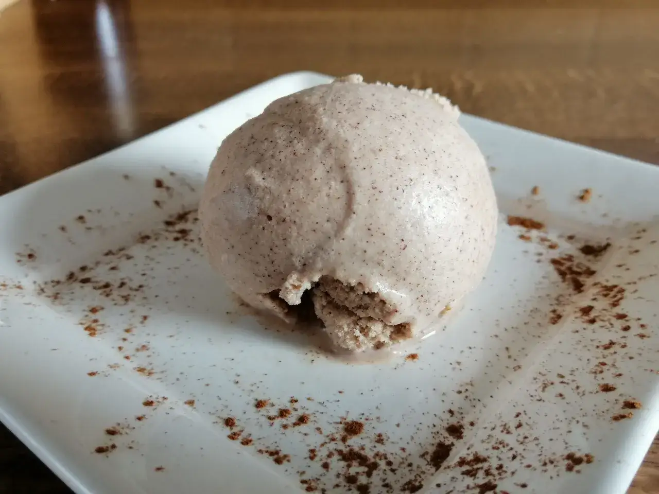 Ein Klacks Zimteis, frisch aus der Eismaschine, auf einem wei&szlig;en Teller mit Zimt bestreut.