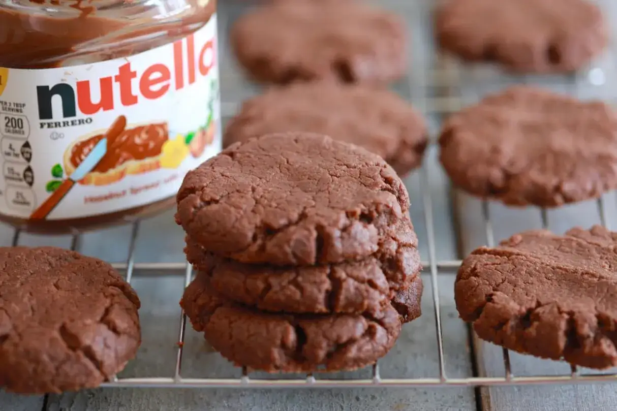 Ein Glas Nutella neben einem Stapel frisch gebackener Nutella-Kekse.