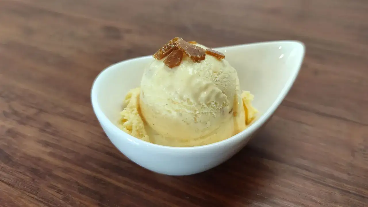 Cremiges Eis mit Eigelb, garniert mit karamellisierten Stückchen, in einer weißen Schale auf Holzhintergrund.