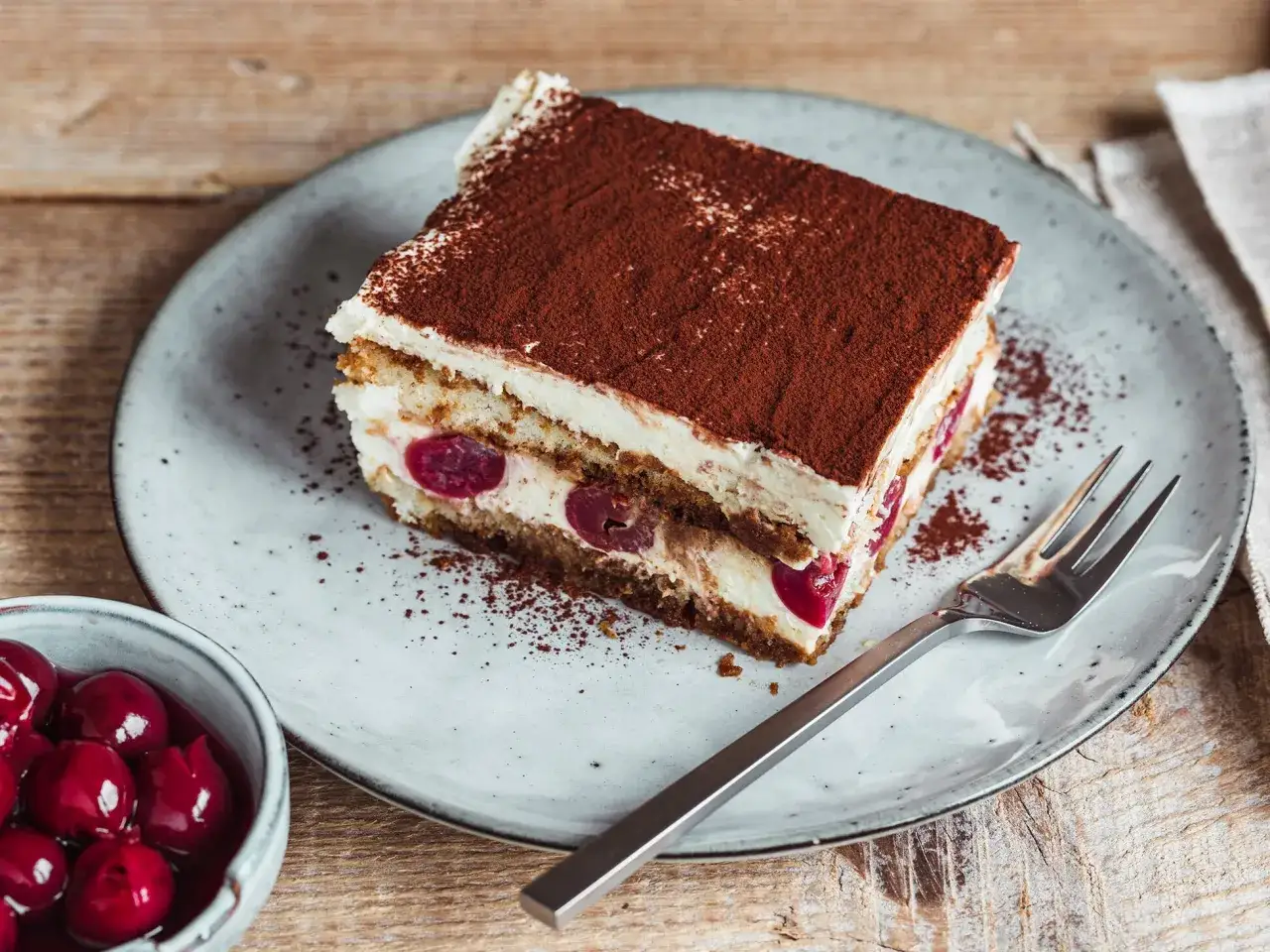 Ein Stück Kirsch-Tiramisu, verfeinert mit Kakaopulver. Perfekt für alle, die nach neuen Tiramisu Rezepte suchen.