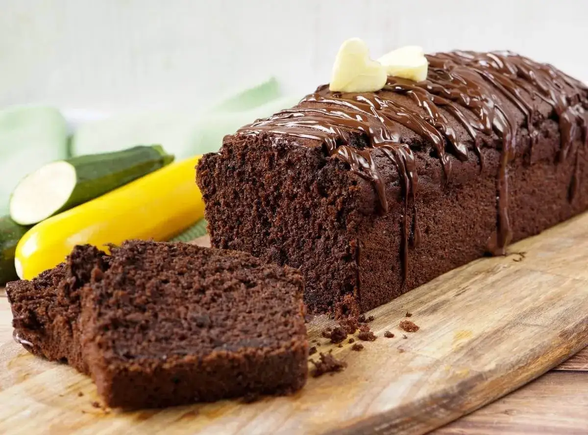 Saftiger Zucchini Schoko Kuchen mit Schokoladenglasur und Herz-Dekoration, daneben Zucchini und gelbe Zucchini.