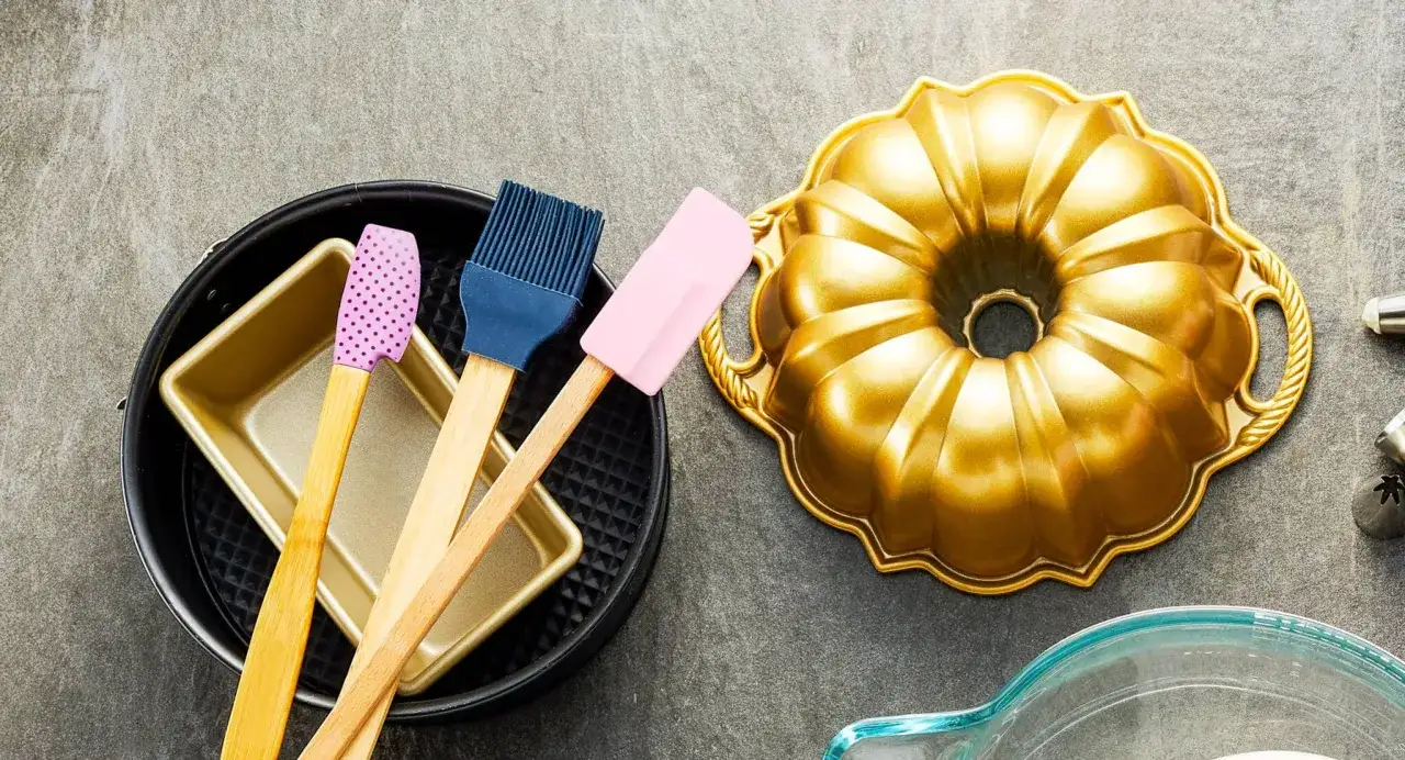 Backutensilien für den perfekten Kuchen: goldene Gugelhupfform, Backformen, Pinsel und Spatel.