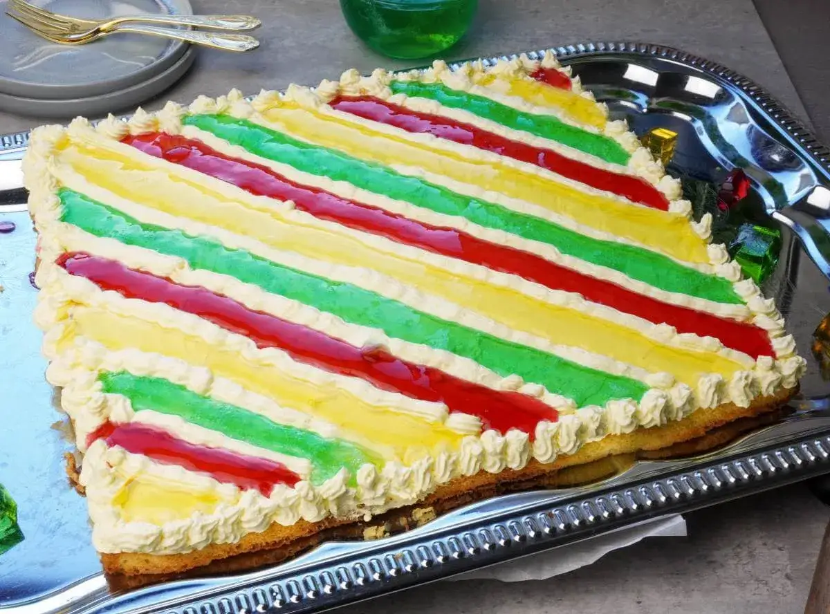 Bunter Geburtstagskuchen für Kinder mit Streifen aus roter, gelber und grüner Glasur, verziert mit Sahnetuffs.