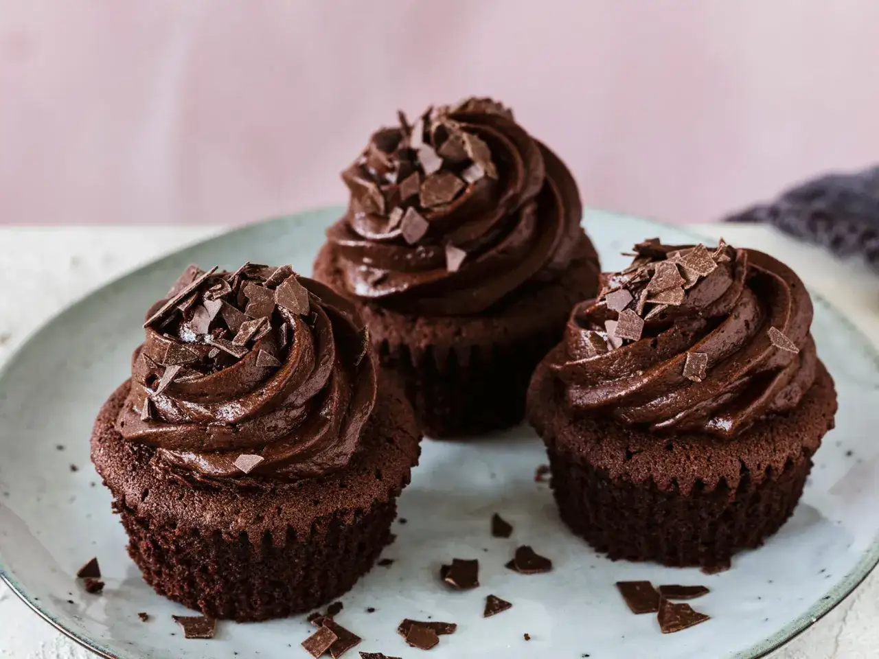 Drei schoko cupcakes mit dunkler Schokoladencreme und Schokostückchen auf einem Teller.