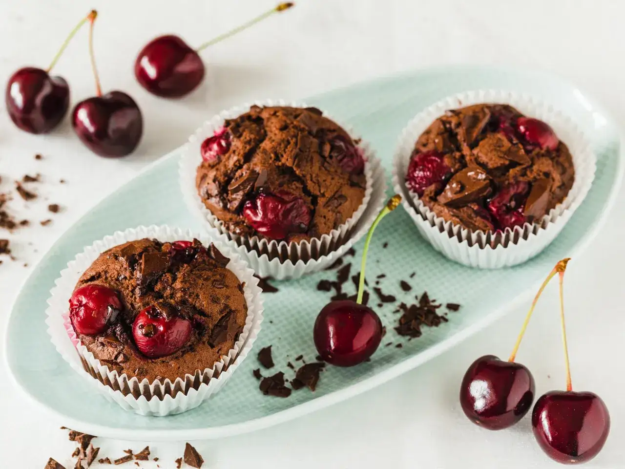 Schoko Kirsch Muffins mit saftigen Kirschen und Schokostückchen, garniert mit frischen Kirschen und Schokosplittern.