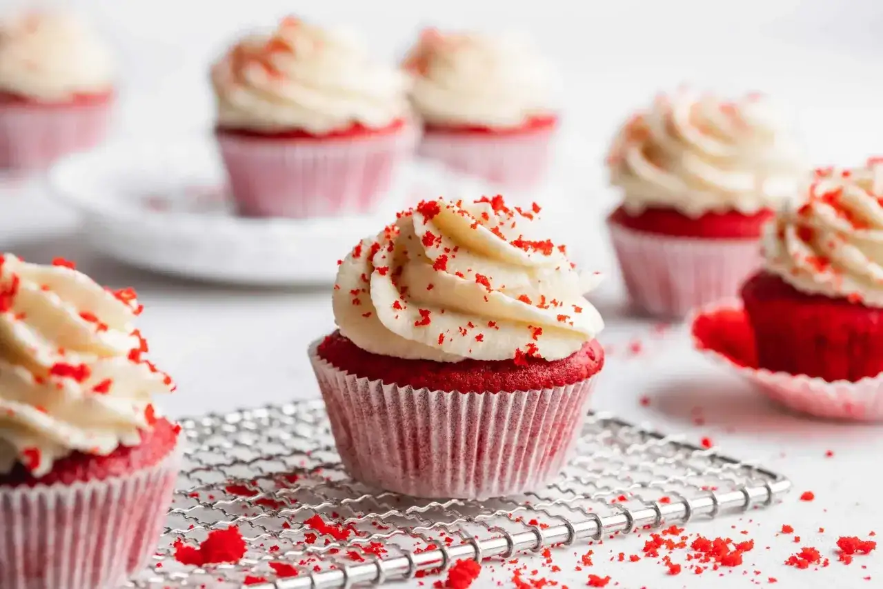 Mehrere rote Samt-Cupcakes mit weißem Zuckerguss und roten Krümeln.