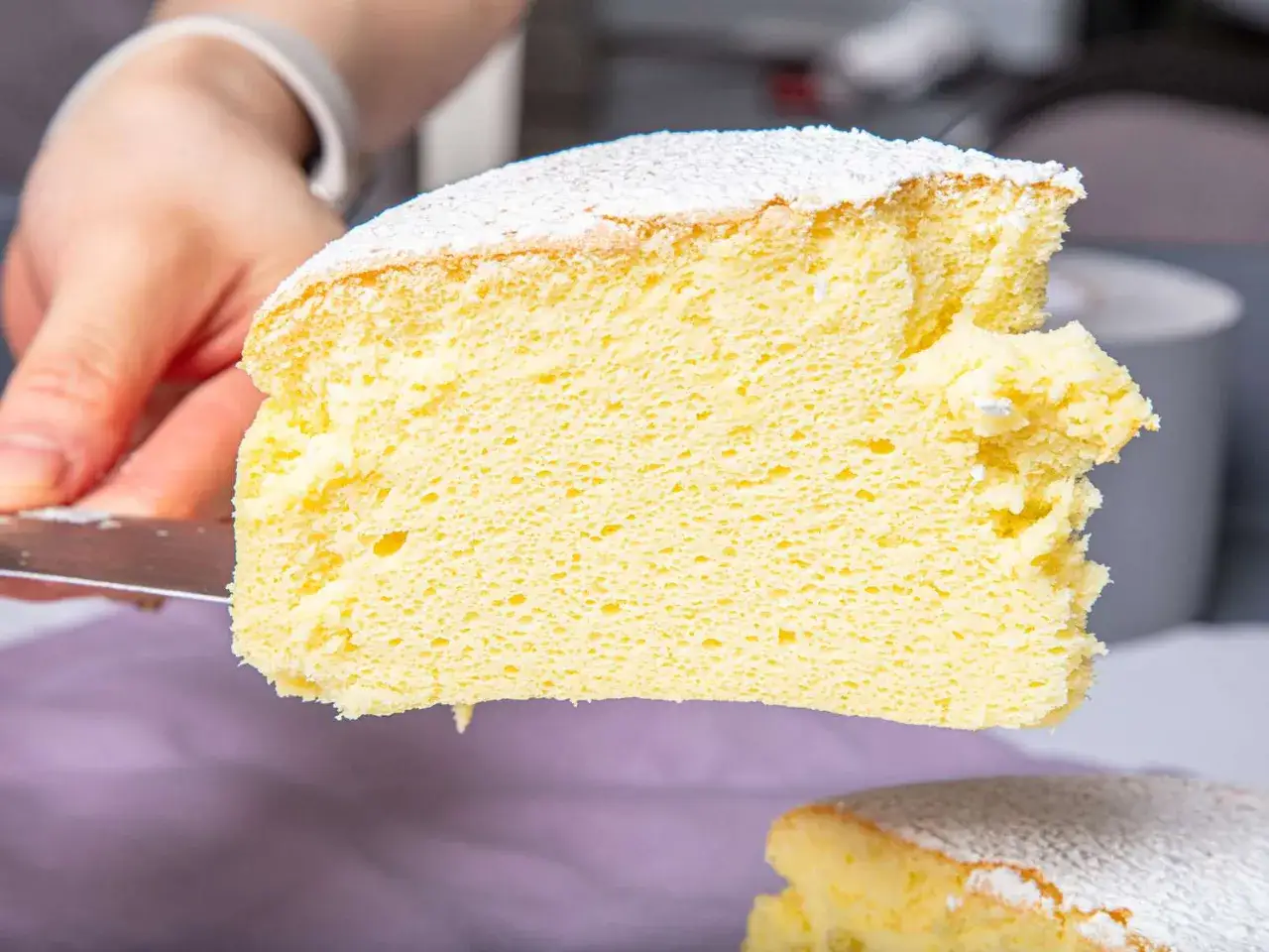 Ein St&uuml;ck luftiger, fluffiger japanischer Cheesecake wird mit einem Messer herausgeschnitten, best&auml;ubt mit Puderzucker.