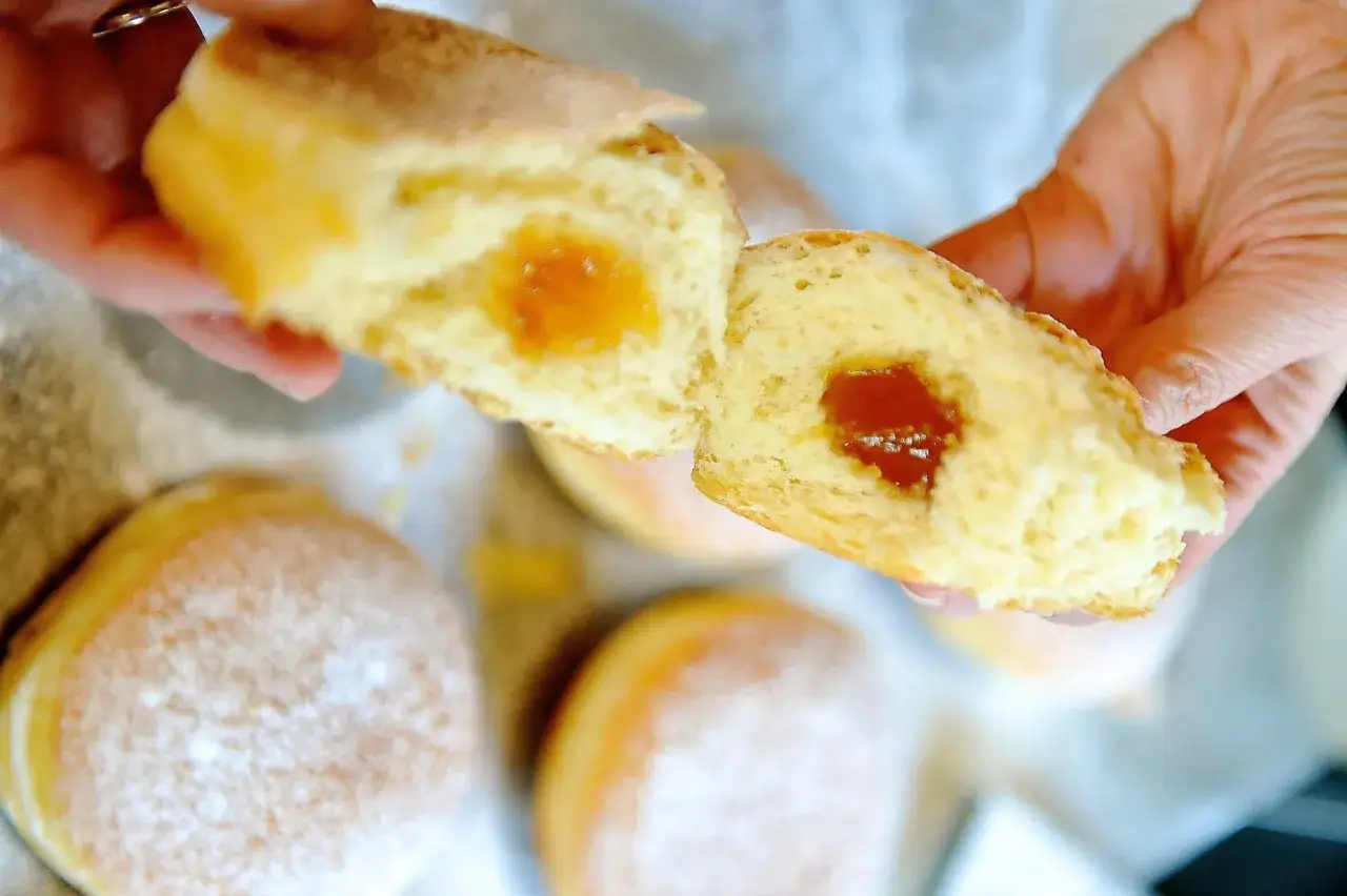 Ein Krapfen wird auseinandergebrochen, das Innere mit Marmelade ist sichtbar. Ein k&ouml;stliches Krapfen Rezept zum Nachbacken.
