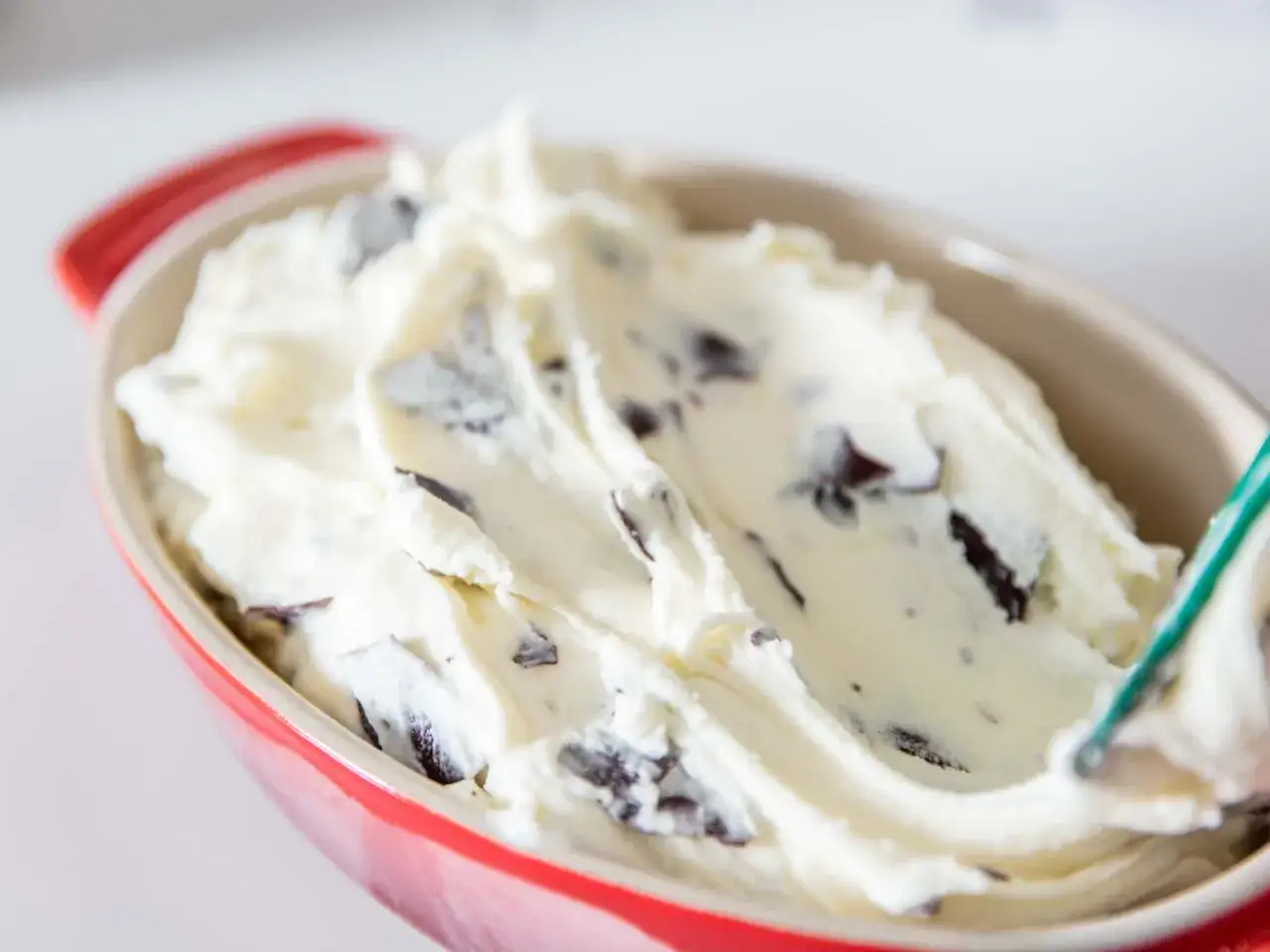 Cremiges Stracciatella Eis mit dunklen Schokoladenstückchen in einer roten Schale, bereit zum Genießen.