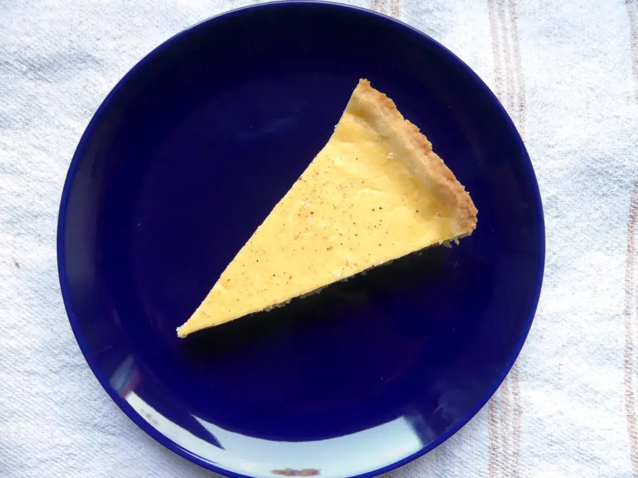 Ein Stück Torta della Nonna, ein cremiger Kuchen mit Zitronengeschmack, auf einem blauen Teller.