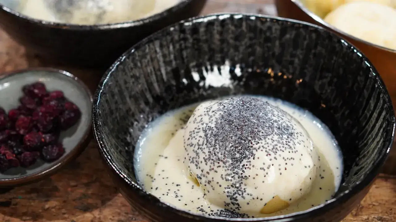 Ein Dampfnudel-Rezept, das fluffige Dampfnudeln in Vanillesauce mit Mohn bestreut zeigt. Daneben eine Schale mit Cranberries.