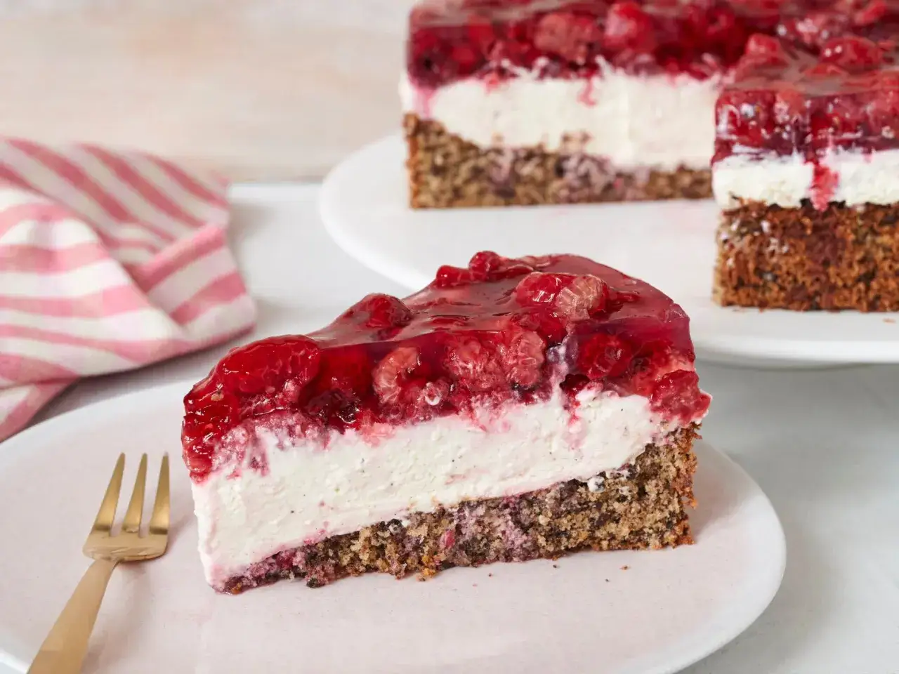 Ein Stück Himbeer Mascarpone Torte mit cremigem Frischkäse, fruchtiger Himbeerschicht und nussigem Boden.