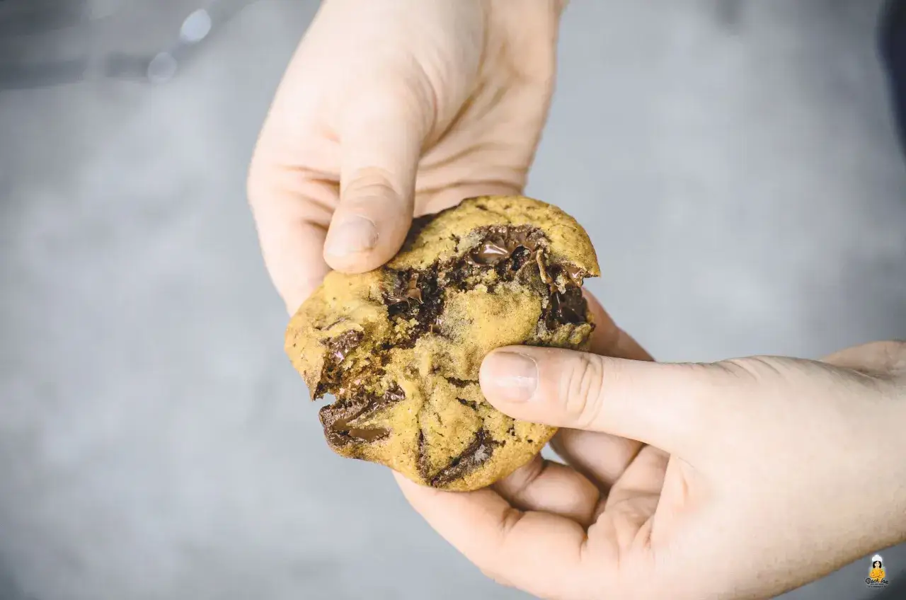 Hände halten einen frisch gebackenen Chocolate Chip Cookie, der gerade auseinandergebrochen wurde. Perfekt für alle, die Cookies selber machen wollen!