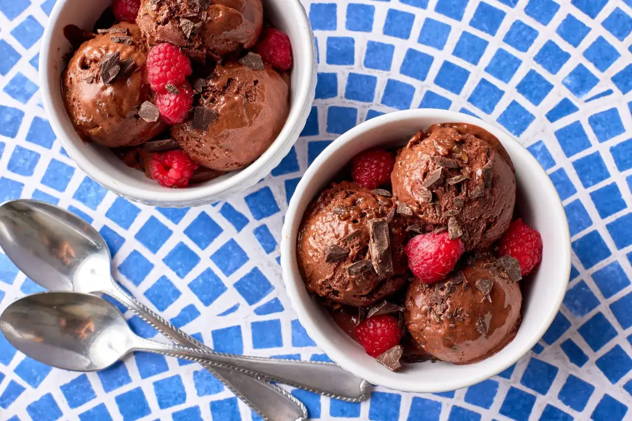 Zwei Schalen mit cremigem Schokoladen-nice-cream, garniert mit Himbeeren und Schokost&uuml;ckchen, daneben zwei L&ouml;ffel.