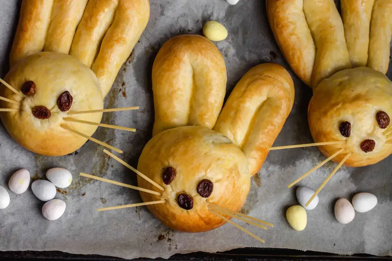 Osterhasen backen mit Hefeteig: Süße Hasen aus Teig mit Rosinenaugen und Spaghetti-Schnurrhaaren, umgeben von bunten Zuckereiern.