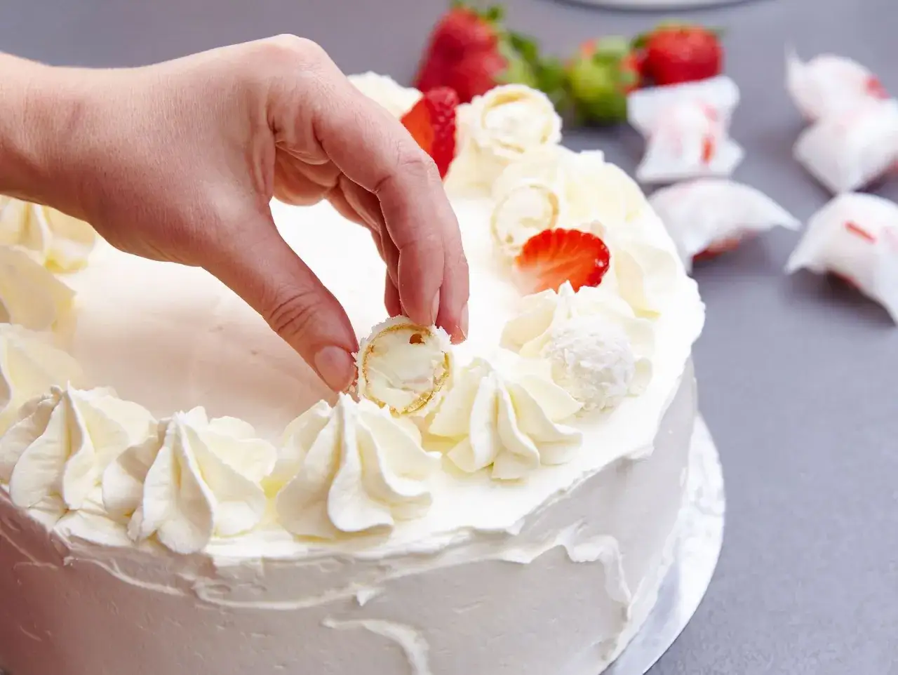 Eine Hand dekoriert eine Erdbeer Raffaello Torte mit Sahnetuffs und frischen Erdbeeren.