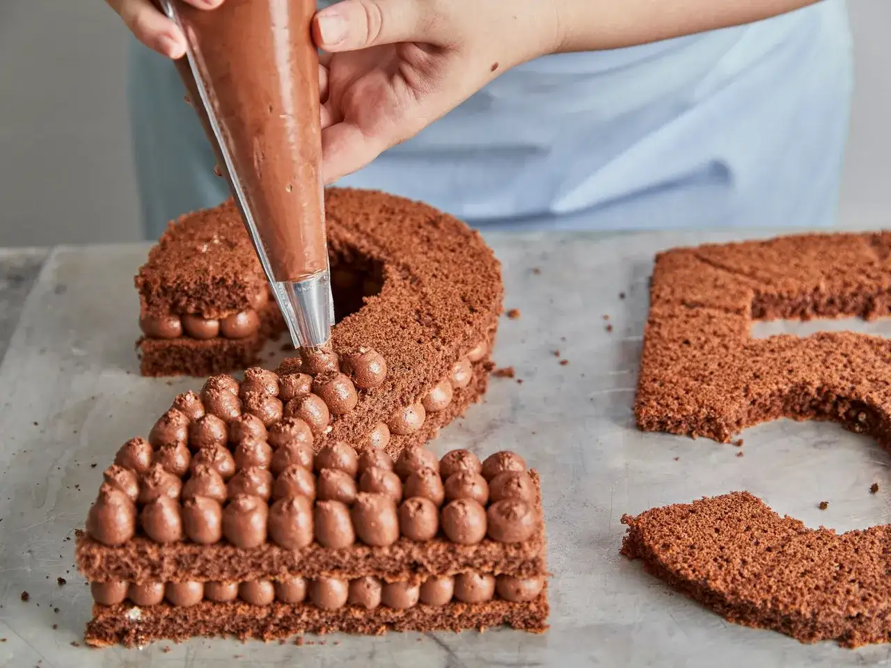 Eine Zahlentorte mit Biskuitboden wird mit Schokoladencreme verziert. Die Zahl 2 ist fast fertig, die 5 liegt daneben.