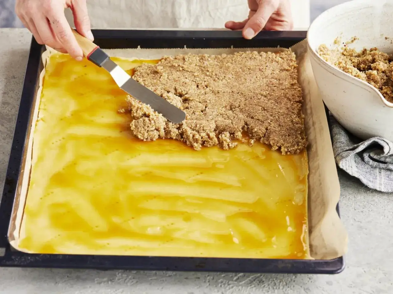 Eine Teigschicht mit goldgelber Füllung wird mit einer Nussmasse für vegane Nussecken bedeckt.
