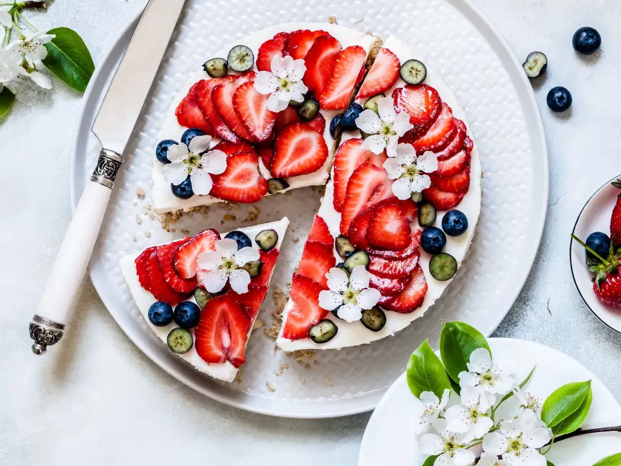 Ein köstlicher no bake cheesecake, dekoriert mit frischen Erdbeeren, Blaubeeren und zarten Blüten.