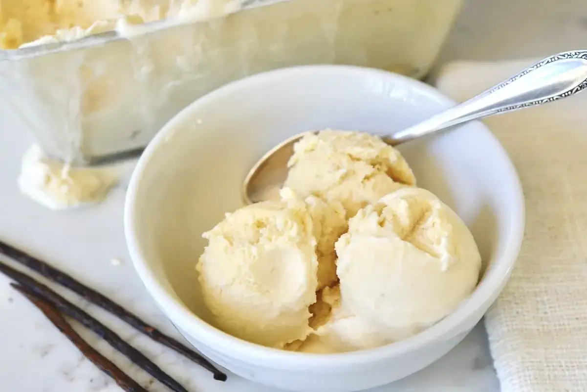 Cremiges Eis mit Milch statt Sahne, serviert in einer Schüssel mit Löffel und Vanilleschoten.
