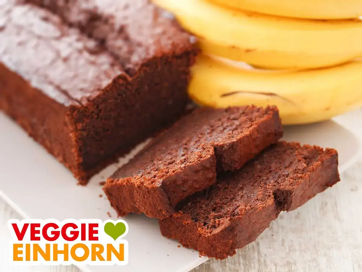Saftiger veganer Bananenkuchen, schokoladig und lecker. Daneben liegen reife Bananen.