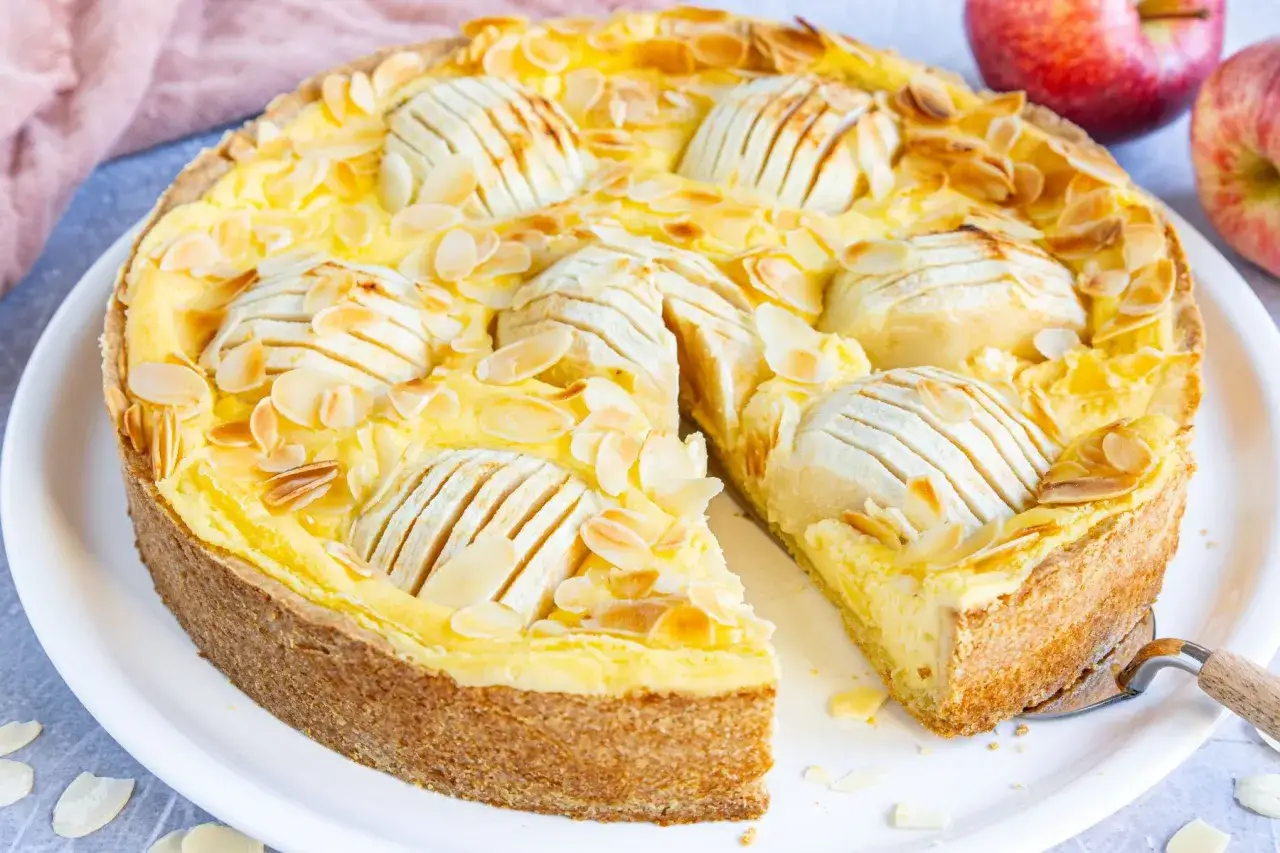 Saftiger Apfel-Schmand-Kuchen mit Mandelsplittern und einer angeschnittenen Scheibe.