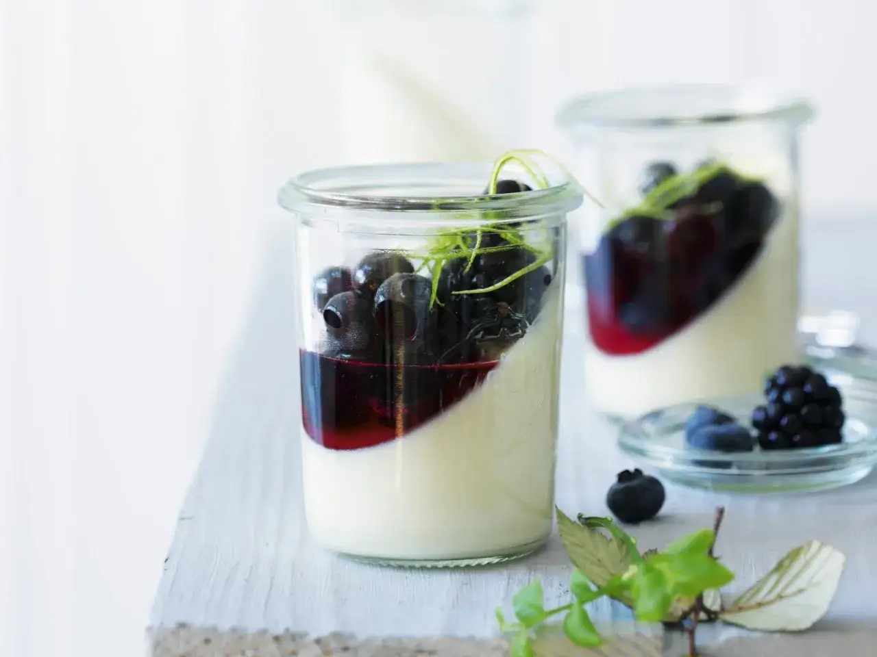 Zwei Gläser Panna Cotta mit Blaubeersauce und Limettenzesten. Ein einfaches panna cotta rezept für Genießer.