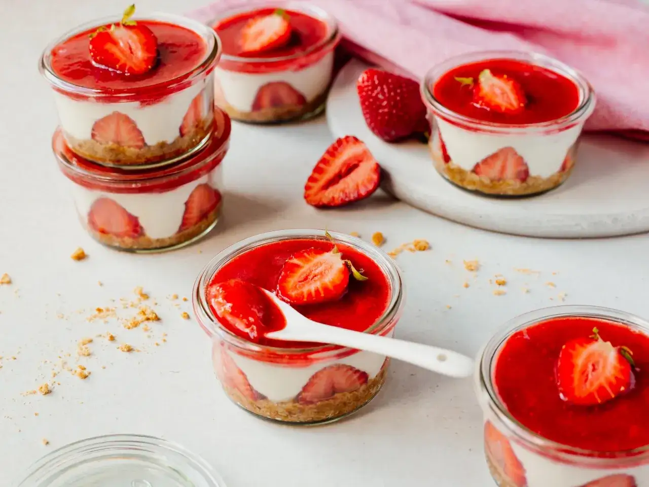 Mehrere Erdbeer-Desserts im Glas mit Frischk&auml;secreme, Erdbeeren und rotem Fruchtp&uuml;ree, garniert mit Erdbeerscheiben.