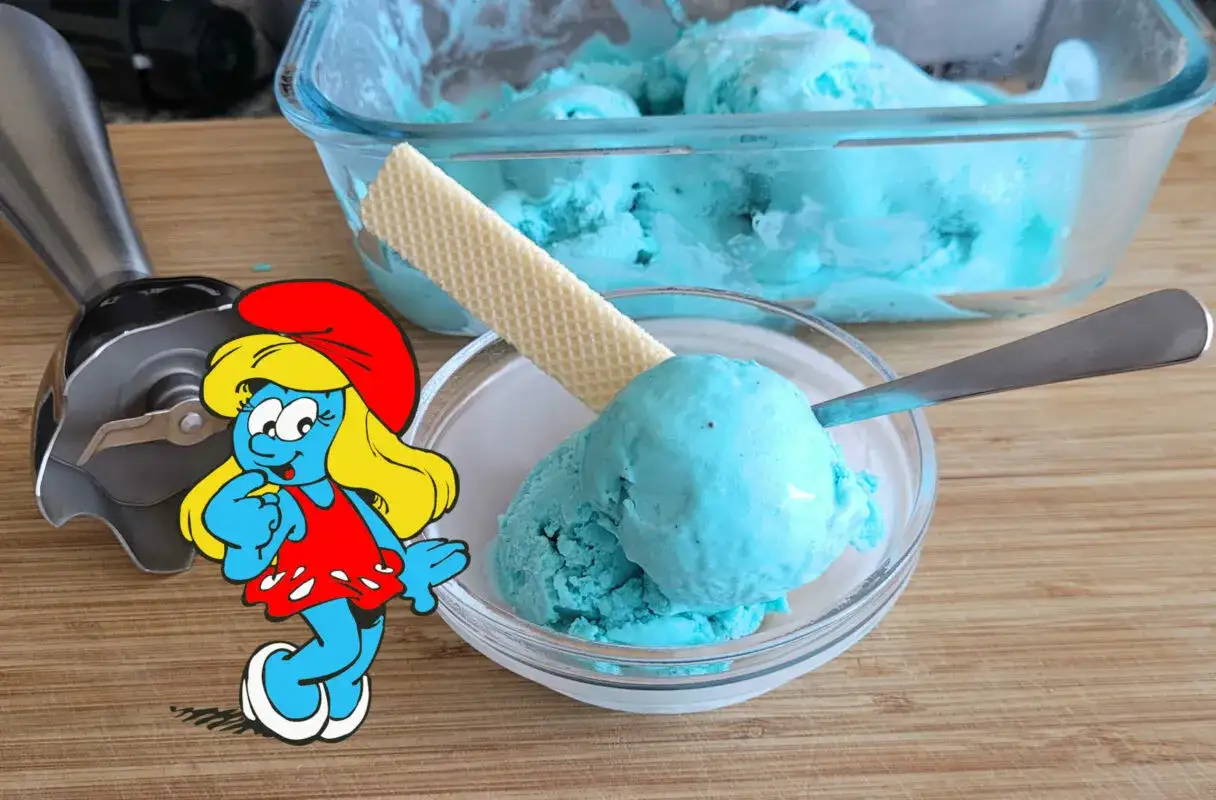 Ein Schüsselchen mit blauem Eis, garniert mit einer Waffel. Ein Mixer und eine kleine Schlümpfin stehen daneben.