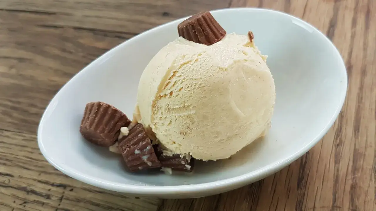 Cremiges Erdnussbutter Eis mit Schokoladenstückchen in einer weißen Schale auf Holzhintergrund.