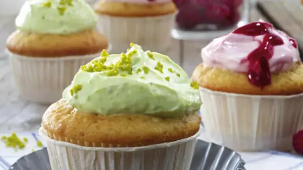 Zwei Cupcakes mit cremiger, grüner Pistazien-Frosting und ein weiterer mit rosa Beeren-Frosting.