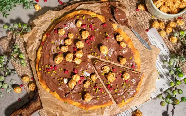 Eine köstliche Nutella Pizza, belegt mit karamellisiertem Popcorn und gehackten Pistazien, bereit zum Genießen.