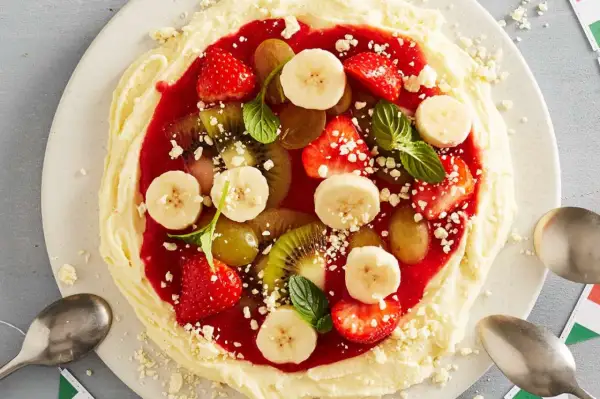 Fruchtige eis pizza mit Erdbeeren, Bananen, Kiwi und Trauben auf cremigem Boden, garniert mit Minze.