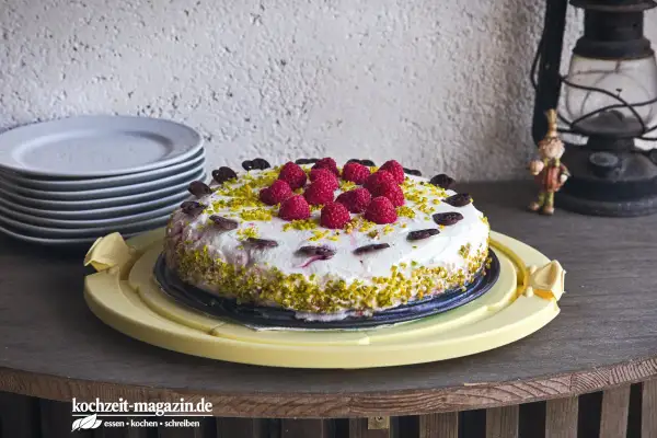 Himbeer Torte mit frischen Beeren, gehackten Pistazien und Schokoladenherzen verziert. Ein Genuss für jeden Anlass.