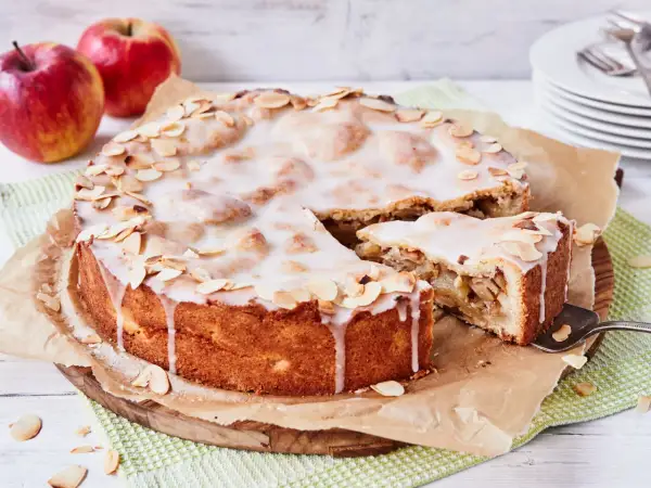 Ein köstlicher gedeckter Apfelkuchen mit zarter Glasur und Mandelblättchen, daneben ein Stück Apfelmus.