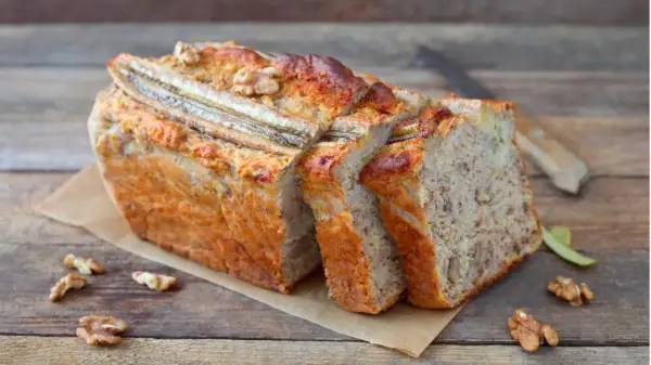 Saftiger bananenkuchen vegan, mit Nüssen und Bananenstücken, auf einem Holztisch.