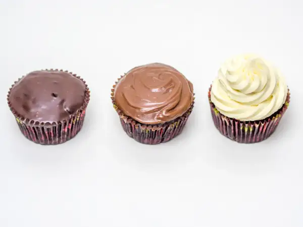 Drei Cupcakes: einer mit dunkler Ganache, einer mit Milchschokoladen-Ganache und einer mit weißer Creme. Perfekt für ein schnelles Ganache Rezept.