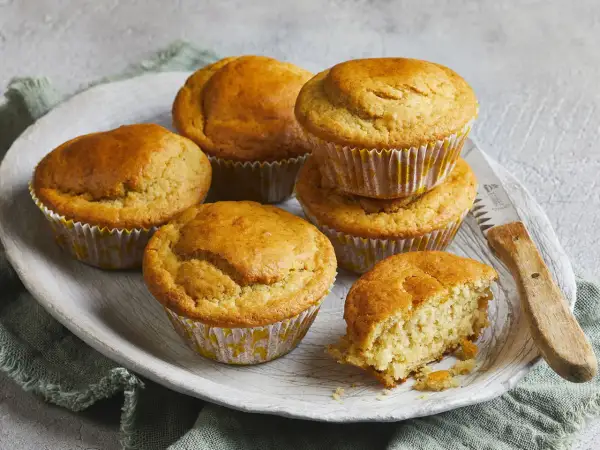 Goldbraune Buttermilch Muffins auf einem Holzteller, einer davon angebrochen, mit einem Messer daneben.