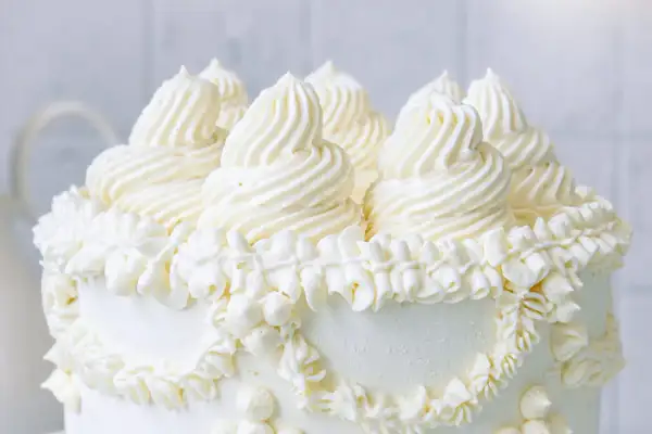 Eine üppige Buttercreme Torte mit kunstvollen Tupfen und Rüschen aus weißer Buttercreme, die auf einem weißen Hintergrund steht.