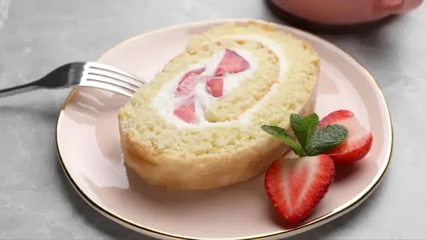 Ein Stück Biskuitrolle mit Erdbeeren und Sahne, perfekt für ein leichtes Dessert. Dieses Biskuitrolle Rezept ist ein Genuss!