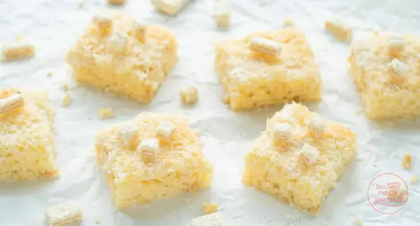 Saftige Stücke Buttermilch Kokos Kuchen, bestreut mit Kokosraspeln und kleinen weißen Würfeln, verlocken zum Genuss.