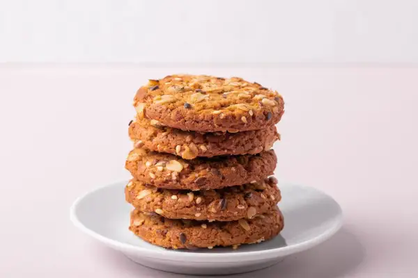 Ein Stapel knuspriger Kekse ohne Zucker, verfeinert mit Haferflocken und Samen, auf einem weißen Teller.
