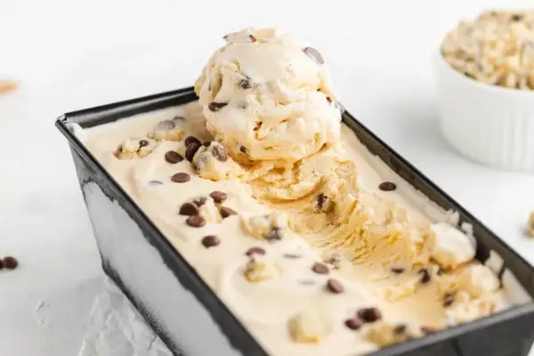 Cremiges Cookie Dough Eis mit Schokoladenstückchen in einer schwarzen Form, eine Kugel ist herausgenommen.
